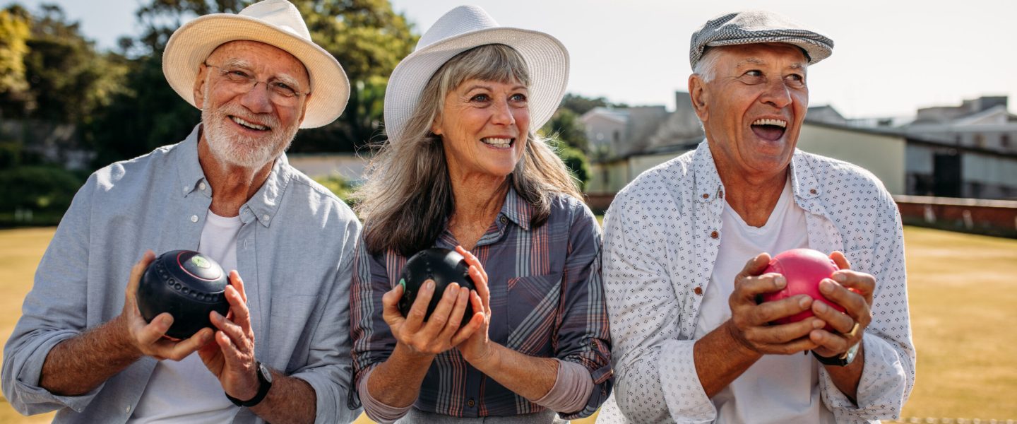 Three senior persons sitting in a park holding boules in their hands. Cheerful senior men and a woman having fun sitting outdoors enjoying the game of boules.